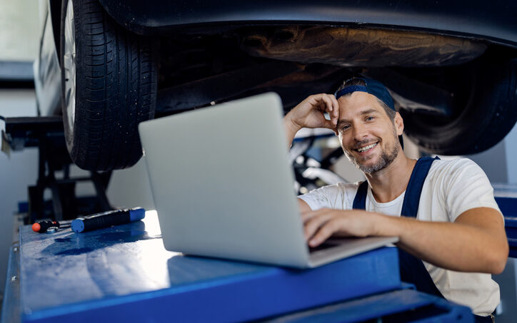 Happy repairman using computer while working at car workshop