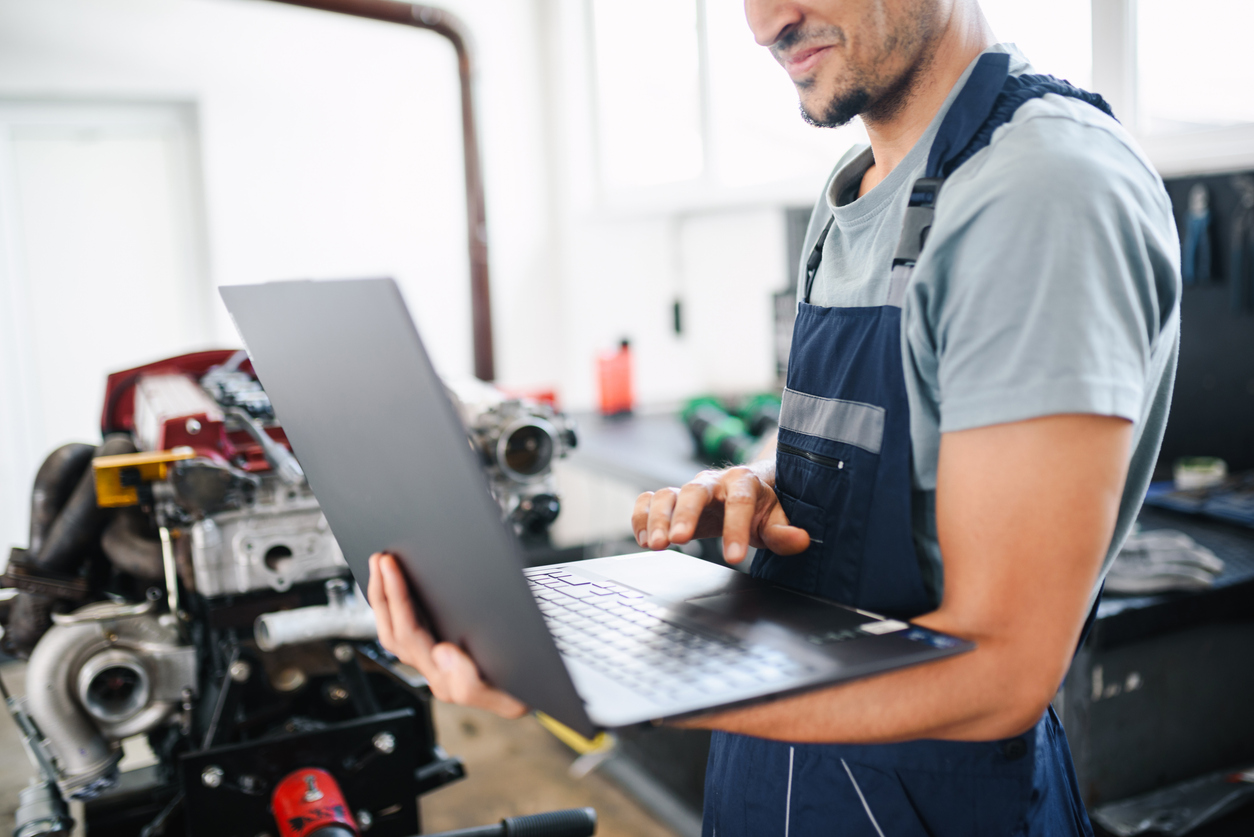 Young car mechanic in his auto repair shop using laptop for digital diagnosis