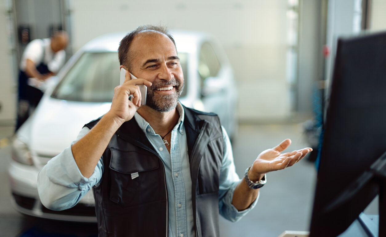 Happy mechanic making a phone call while working at auto repair shop