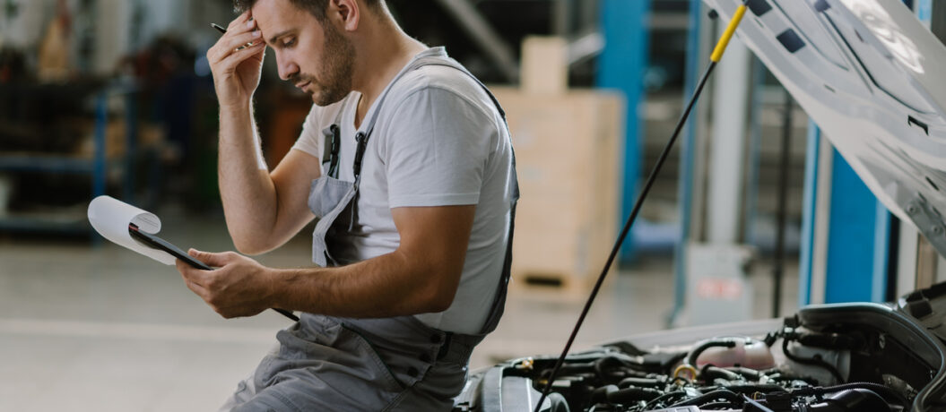 Young auto mechanic seeing potential problems while working on reports in a workshop