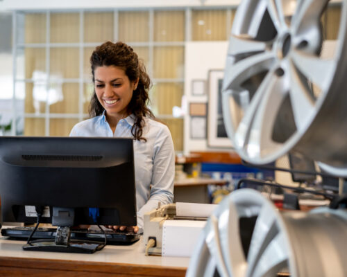Beautiful woman working at the reception of an auto repair shop looking at computer screen very cheerfully  and smiling