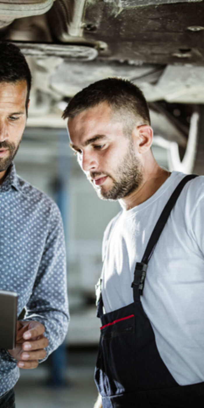 Male customer and mechanic cooperating while using digital tablet in auto repair shop.