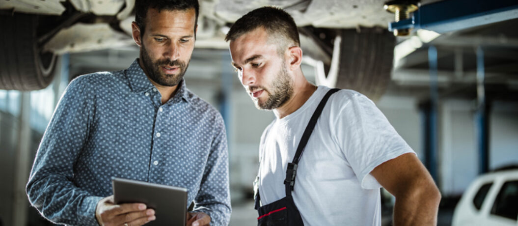 Male customer and mechanic cooperating while using digital tablet in auto repair shop.