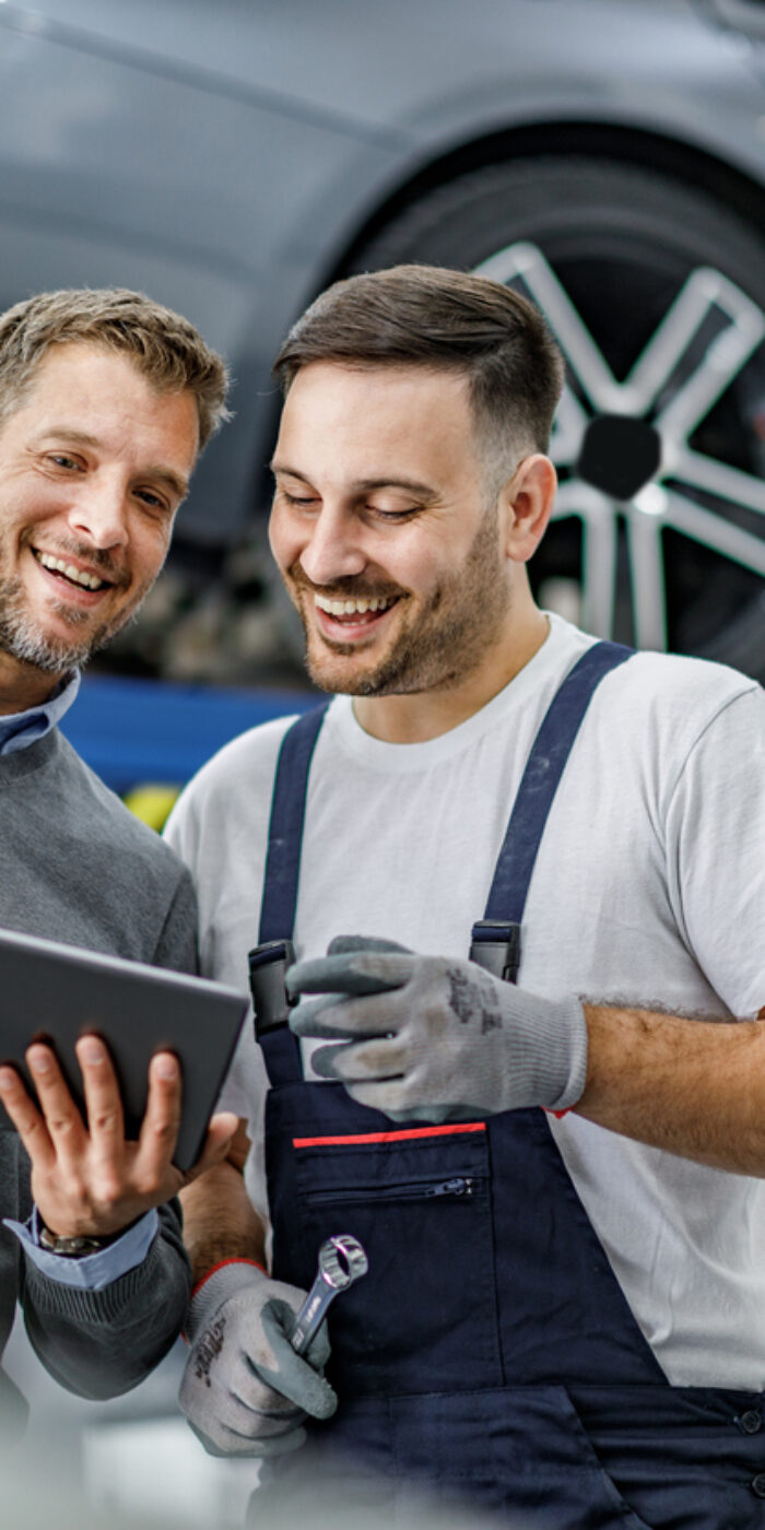 Happy manager and auto mechanic cooperating while using digital tablet in a repair shop.
