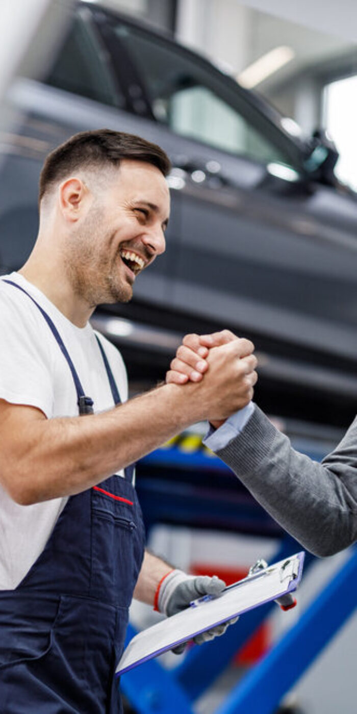 Happy mechanic and his foreman greeting each other with a manly handshake in auto repair shop.
