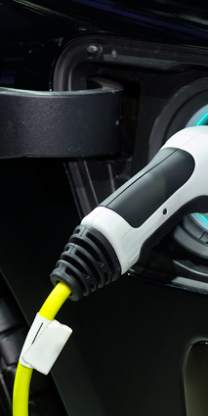 Close-up hand grip plug of industrial electric charging machine connected with socket  charge on black modern car for rechargeable battery, zero emission vehicle (ZEV) and green energy for smart life